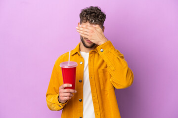 Fototapeta premium Young blonde man holding soda isolated on purple background covering eyes by hands. Do not want to see something