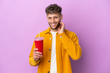Fototapeta premium Young blonde man holding soda isolated on purple background laughing