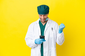 Surgeon blonde man in green uniform isolated on yellow background surprised and sending a message