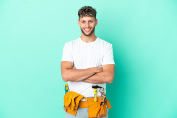 Young electrician blonde man isolated on green background keeping the arms crossed in frontal...