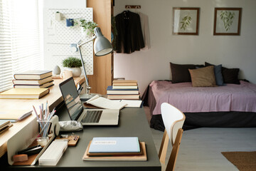 Contemporary interior of students room furnished with bed and desk full of books and supplies