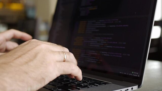 Close-up of male hands typing code on silver notebook keyboard. A caucasian young man works on a laptop in a cafe or coworking space