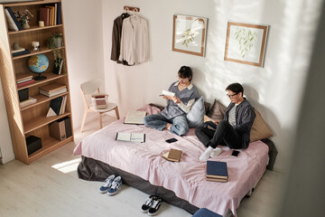 Asian student couple sitting on bed with books and preparing for exam together
