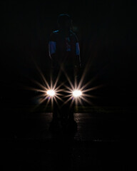 Fototapeta premium a young man stands in front of car headlights forming a star pattern on a dark night
