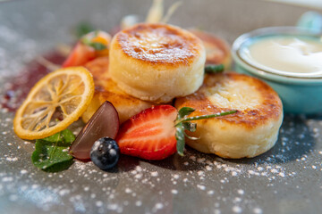 Cheesecakes with condensed milk and strawberries on a gray plate standing on a dark table
