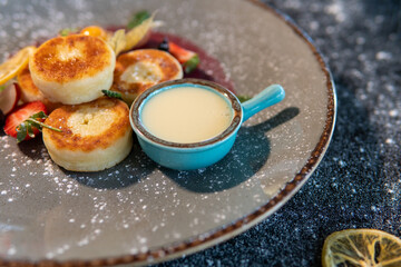 Cheesecakes with condensed milk and strawberries on a gray plate standing on a dark table