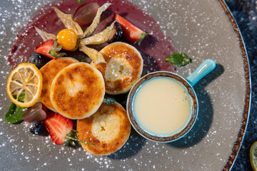 Cheesecakes with condensed milk and strawberries on a gray plate standing on a dark table