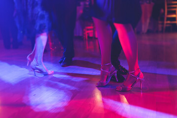 Dancing shoes of a couple, couples dancing traditional latin argentinian dance milonga in the ballroom, tango salsa bachata kizomba lesson, festival on a wooden floor, purple, red and violet lights