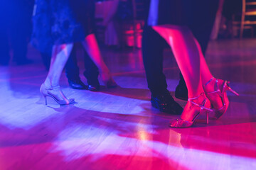 Dancing shoes of a couple, couples dancing traditional latin argentinian dance milonga in the ballroom, tango salsa bachata kizomba lesson, festival on a wooden floor, purple, red and violet lights