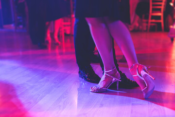 Dancing shoes of a couple, couples dancing traditional latin argentinian dance milonga in the ballroom, tango salsa bachata kizomba lesson, festival on a wooden floor, purple, red and violet lights