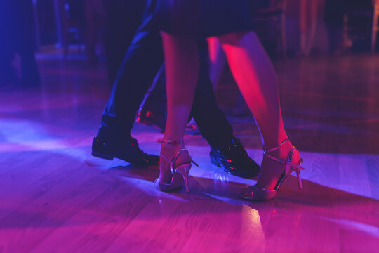 Dancing shoes of a couple, couples dancing traditional latin argentinian dance milonga in the ballroom, tango salsa bachata kizomba lesson, festival on a wooden floor, purple, red and violet lights