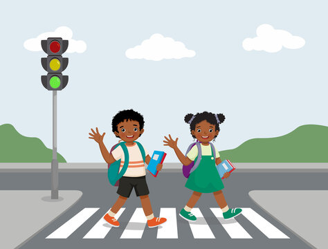 Cute African school kids with backpack waving hands walking crossing road near traffic light on zebra crossing on the way to school