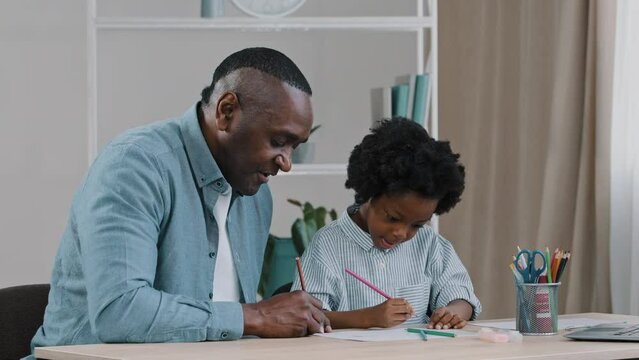 Happy dad with little daughter sitting at desk in cozy living room drawing together father peeping at kid girl picture having fun spending free time giving high five enjoying hobby child development