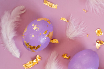 Close up view of dued Easter egg, violet or very peri color with golden foil and feathers on violet background, Easter greeting card.