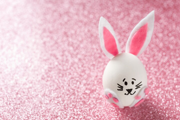 Easter egg decorated as cute bunny on the pink blurred glitter background, copy space. 