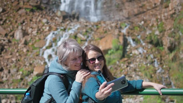 Mother and daughter taking selfie against the waterfall background. Slow motion. 