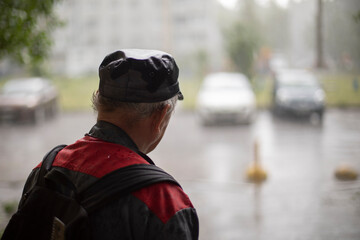 A man looks at the rain. An old man in a cap in bad weather.