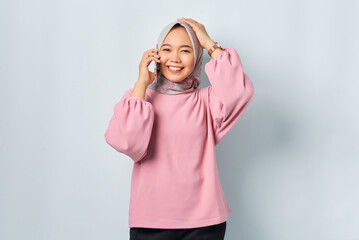 Cheerful young Asian woman in pink shirt talking on mobile phone isolated over white background