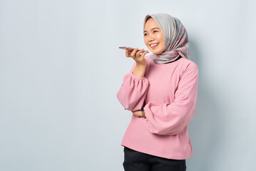 Cheerful young Asian woman in pink shirt using the voice assistant on mobile phone isolated over white background