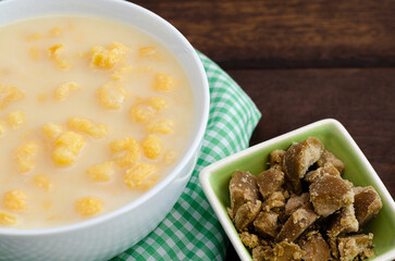 Traditional Colombian food called mazamorra,based on cooked corn dissolved in milk,accompanied with panela in pieces (sweet from sugar cane). Dark wooden background.