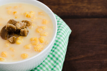 Traditional Colombian food called mazamorra,based on cooked corn dissolved in milk,accompanied with panela in pieces (sweet from sugar cane). Dark wooden background.