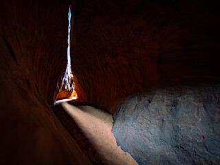 Leprechaun Canyon gets narrow in the Utah desert, then opens up to a beam of light. Light casts down into the sandstone cavern, showing a rock embedded into the sandy floor.