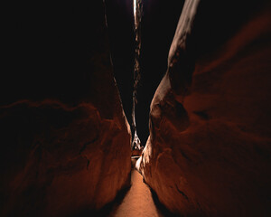 A desert canyon gets narrow, features on the Utah red rocks cast dark shadows as the walls close in. Sandstone cave with light cast down into the crevasse. Looks like sacred a sacred place in Petra