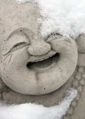 Obraz premium Smiling concrete Buddha statue with snow covering part of its head daytime