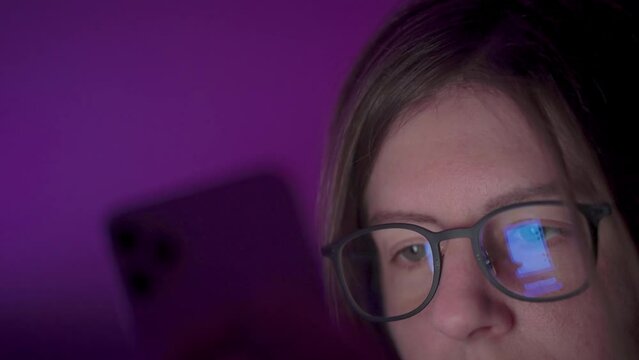 Reflection of phone screen on girl's glasses as she browses social media on smart phone late at night