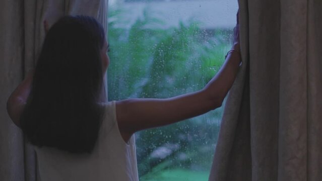 Close up shot of woman removing curtain to see rain from window in Diu city of India.