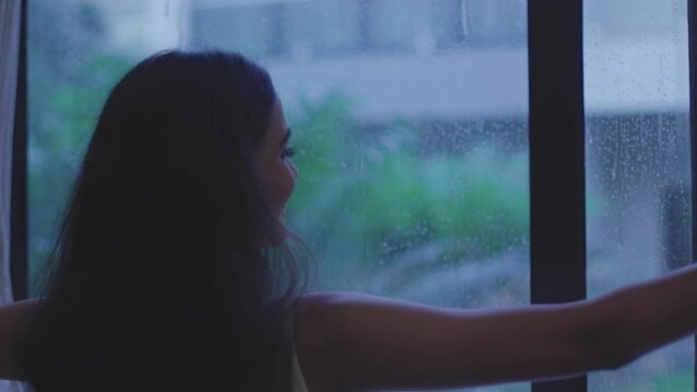 Close up shot of woman removing curtain to see rain from window in Diu city of India.