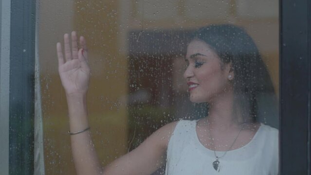 Close up portrait of girl standing near the window while its raining outside at Diu city of India. Bored girl behind window in a rainy day. Shot in 4k