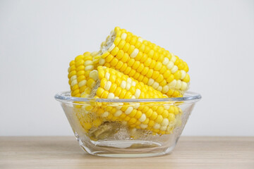 Bowl of corn on the cob (sweet corn, maize) on wooden desk against white wall background, healthy eating concept