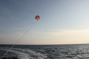 A young man and a girl are flying on a double parachute behind a boat over the sea.