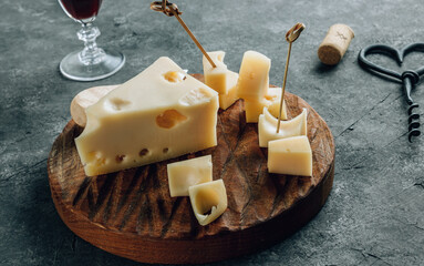 Piece of cow's milk Maasdam cheese on wooden cutting board over concrete background.