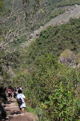 Fototapeta na wymiar Turistas caminham no alto do Huayna Picchu, ao fundo vista das ruinas de Machu Picchu