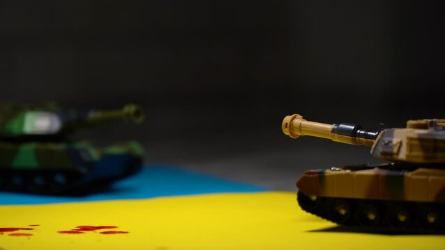 tanks. two toy tanks placed on the flag of Ukraine, drops of red paint dripping on the flag. detail. 4k video.