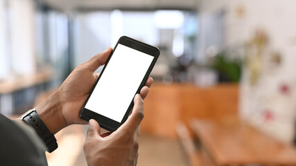 Close up view man hands using smartphone with blurred coffee shop background. Empty screen for graphic display montage.