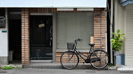 A bicycle with a wicker basket parked on city street in front of brick wall exterior facade of...