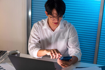 Overwork Concept The male office employee who wears white blazer working late at the office while texting her phone to someone