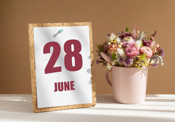 june 28. 28th day of month, calendar date.Bouquet of dead wood in pink mug on desktop.Cork board...