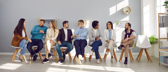 Narrow wide shot of diverse employees sit on chairs in row brainstorm or discuss ideas. Banner of...