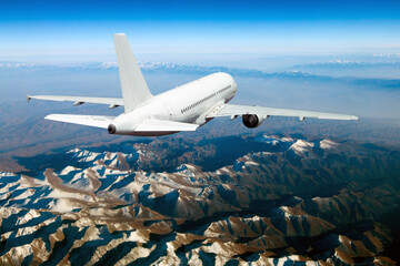 Modern passenger plane flies away. Aircraft fly above the foggy mountain lanscape. Back view.