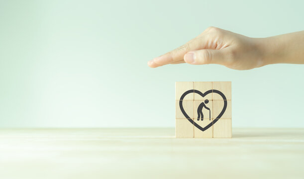 Elderly care concept. Showing hand to protect elderly in wooden cubes. Medical, rehabilitation service, nursing care for enhancing quality of elder age. Nursing home elderly. Background, banner.