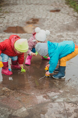 Group of three children in colourful raincoats and rubber boots are playing in the puddle