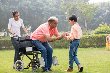 Senior man trying to get up from wheelchair with the help of grandson and granddaughter at park