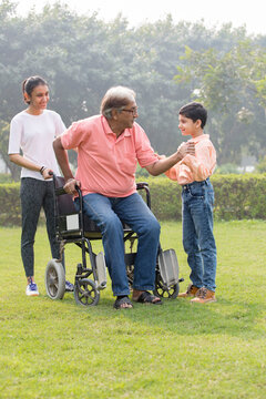 Senior man trying to get up from wheelchair with the help of grandson and granddaughter at park