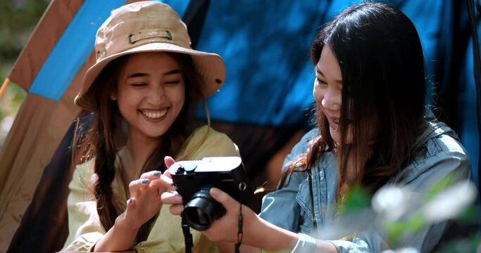 Handheld shot, Young pretty checking photo on camera with girl friends while sitting at the camping tent in forest on holiday vacation, Young Asian group woman travel outdoor camping.