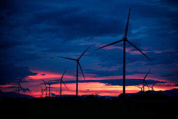 Wind farm or wind park, with high wind turbines in the setting sun for generation electricity with copy space. Green energy concept to reduce climate change and global warming