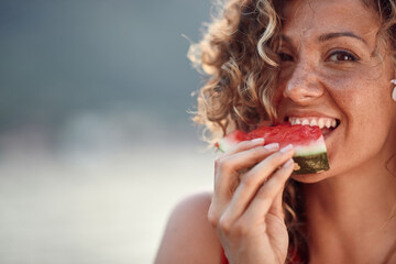 Beautiful young woman with curly hair biting on watermelon piece. Summertime, holiday, lifestyle...
